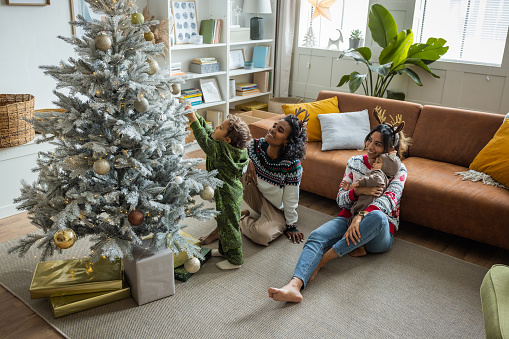 Female gay couple with kids having fun for Christmas at home. They are decorating the Christmas Tree.