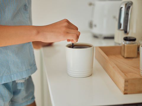 Making fresh, hot and early morning coffee indoors on a kitchen counter to start the day. Hand closeup of preparing a warm beverage and drink inside with a female standing in pajamas at home
