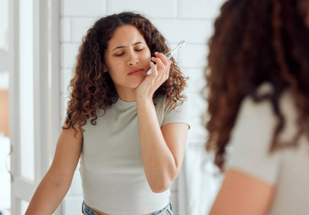 toothache, oral pain and dental sensitivity for a woman brushing her teeth in the morning. african american female suffering with a painful, hurting or inflammation in her mouth in the bathroom - brushing teeth women toothbrush brushing imagens e fotografias de stock