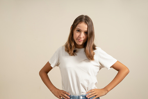 Cute spanish girl with brunette hair looking at camera with arms akimbo, isolated on beige background