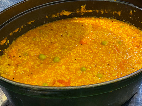 Stock photo showing close-up, elevated view of some freshly made, savoury masala porridge oats in an oven proof dish. This steaming hot porridge has been made with green chillies, ginger, tomato, carrot, beans, peas, bell pepper and coriander leaves, oats, paprika and cumin seeds, turmeric, lemon juice.