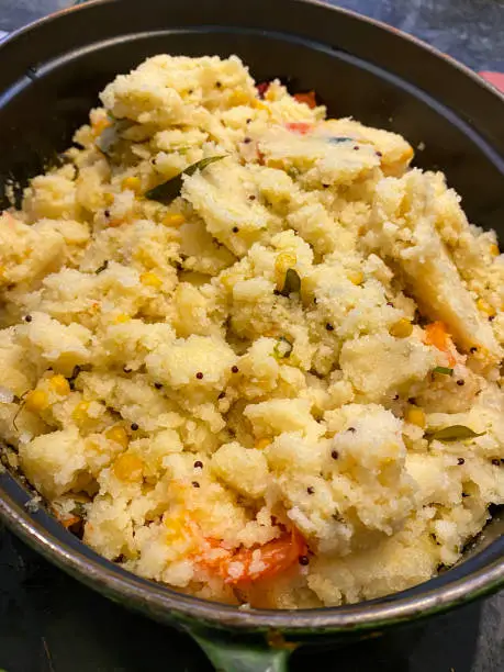 Photo of Close-up image of Indian breakfast recipe of savoury rava upma (semolina) in oven proof serving dish, mustard seed, ghee, chopped onion, ginger, green chillies, lemon juice, sweetcorn, bell pepper, cashew nuts, coriander leaves, elevated view