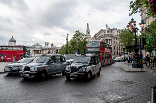 Taxis and buses in a traffic jam in central London. Cars are standing and waiting. People are walking on the sidewalk.