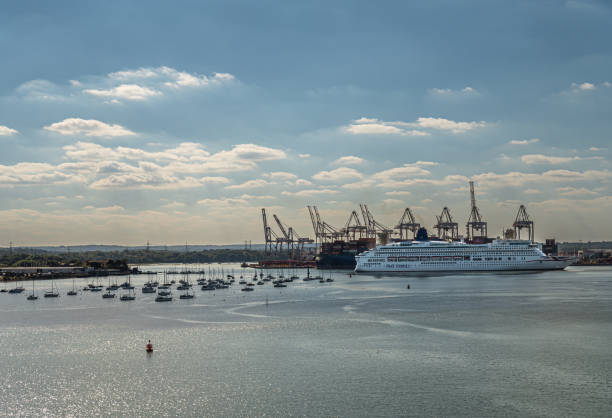 Southampton, England, UK - July 7, 2022: Harbor scenery. White P&O Aurora cruise ship in front of main container terminal under blue cloudscape. Small yachts on gray water up front.