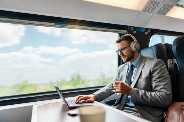 Handsome middle age businessman using his laptop computer while traveling with high speed train. He thoughtfully looking at side. Modern and fast travel concept.