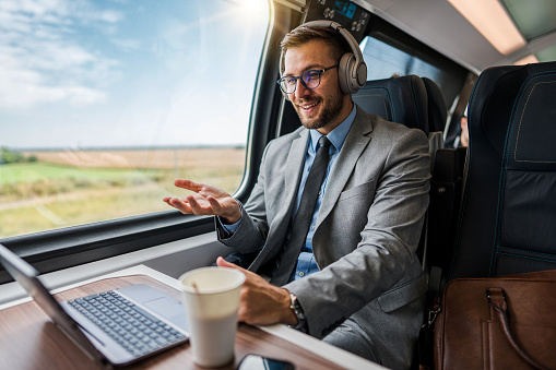 Handsome middle age businessman using his laptop computer while traveling with high speed train. He thoughtfully looking at side. Modern and fast travel concept.