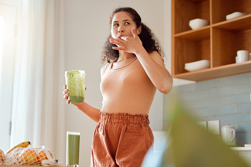 Eating, tasting and drinking a green health smoothie with a young female in a kitchen. Woman on a weight loss, organic and fresh fruit and food diet for wellness, nutrition and a healthy lifestyle