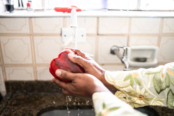 Man's hands washing a red bell pepper in the kitchen