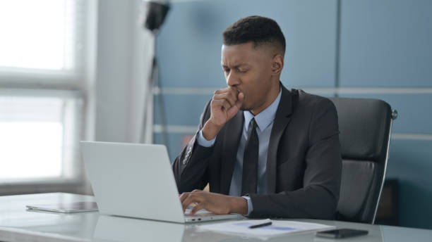 istock African Businessman Coughing while using Laptop in Office 1422027395