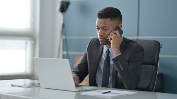 istock African Businessman Talking on Smartphone while using Laptop in Office 1422027509
