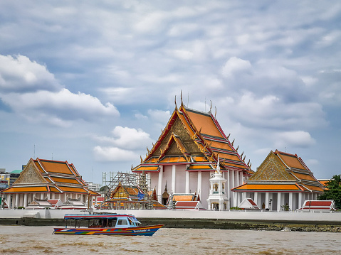 Bangkok, Thailand - September 10, 2019: Wat Kalayanamit Woramahawihan temple with a ferry in front sailing the Chao Phraya river