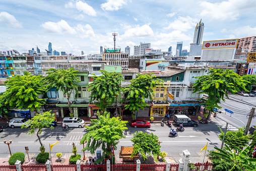 Bangkok, Thailand - September 10, 2019:  cityscape of Bangkok old town during day, with street full of trees,  from Wat Traimit Withayaram Worawihan. In the background is a tall building in the business district