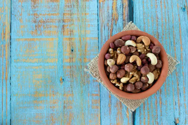 Healthy nut mix (hazelnuts, cashews, almonds, walnuts, peanuts) in a bowl on a rustic wooden background with copy space. Top table view.