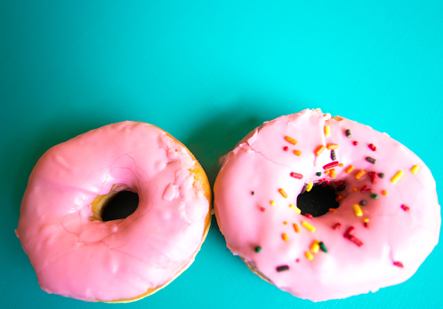 Two Glazed Pink Doughnuts with Sprinkles, Turquoise Background