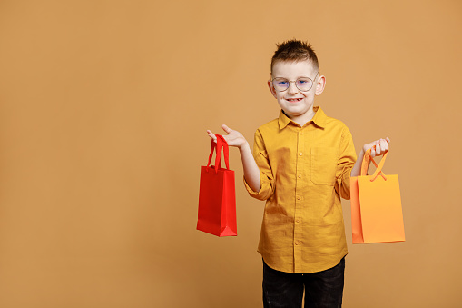 Shopping on black friday. Little boy holding shopping bags on yellow background. Shopper with many colored paper bags. Holidays sales and discounts. Cyber monday. High quality photo.