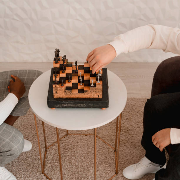 istock Unrecognizable black and white skinned persons play chess boardgame on a small coffee table in the living room at home 1422049578