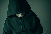 A portrait of an anonymous hacker wearing a mask and a black hoodie sitting bear and scary. Hacking and malware concept.