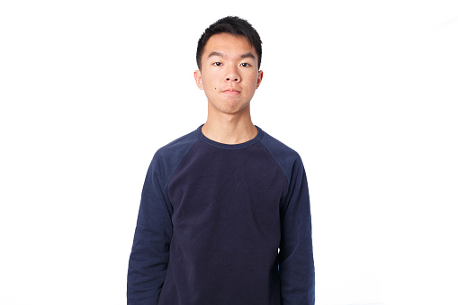 Medium shot of a young teen Asian boy in the studio with flash lighting. He is looking seriously at the camera with a light smile. He is wearing a navy blue sweater. The background is white.