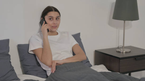 istock Hispanic Woman Talking on Call on Smartphone in Bed 1422099882