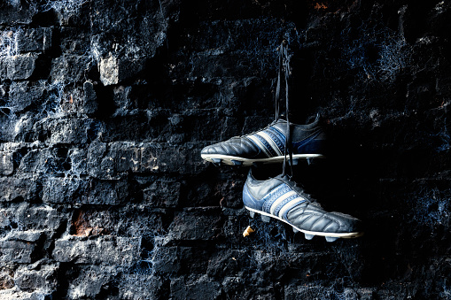 Soccer shoes hanging on a dirty brick wall.