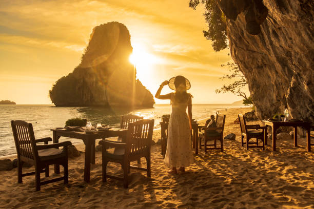 Woman tourist in white dress dinner in restaurant cave on Phra nang Beach at sunset, Railay, Krabi, Thailand. vacation, travel, summer, Wanderlust and holiday concept Woman tourist in white dress dinner in restaurant cave on Phra nang Beach at sunset, Railay, Krabi, Thailand. vacation, travel, summer, Wanderlust and holiday concept exclusive travel stock pictures, royalty-free photos & images