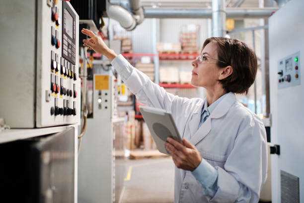 Woman with tablet working with industrial machine at factory stock photo
