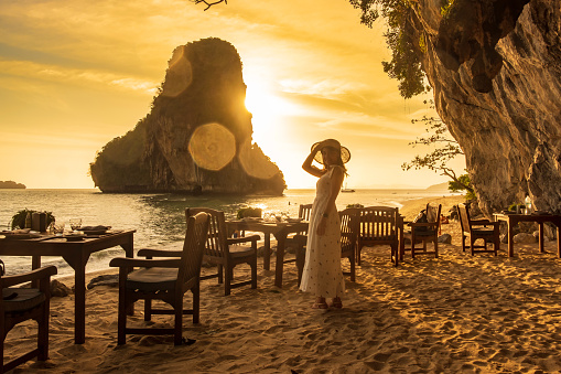Woman tourist in white dress dinner in restaurant cave on Phra nang Beach at sunset, Railay, Krabi, Thailand. vacation, travel, summer, Wanderlust and holiday concept