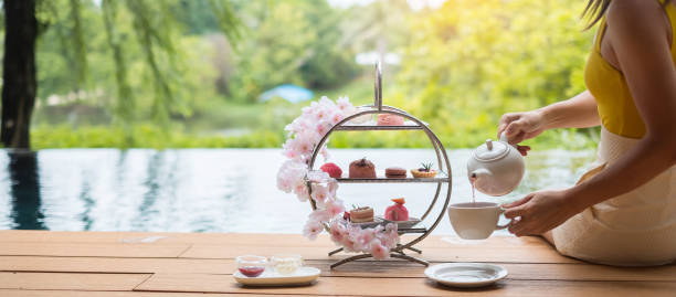 kobieta ręcznie nalewająca gorącą herbatę z popołudniowym zestawem do herbaty i różowym deserem w luksusowym hotelu - afternoon tea tea women table zdjęcia i obrazy z banku zdjęć