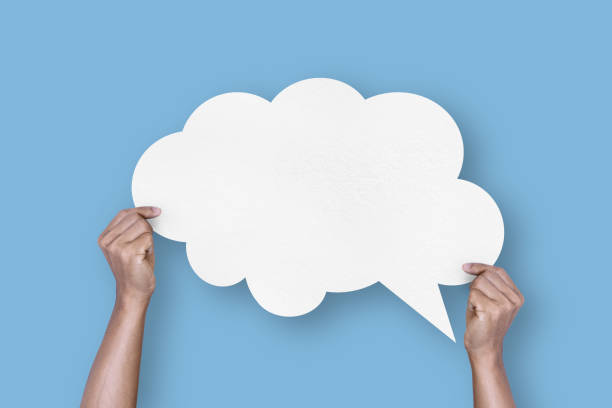 istock hand holding white paper cloud shape speech bubble balloon isolated on light blue background. 1422115473