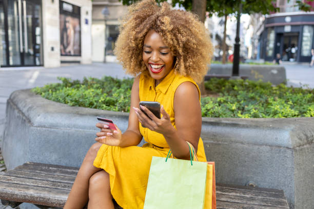 mulher bonita rindo ao fazer compras online - spending money adult african ethnicity bag - fotografias e filmes do acervo