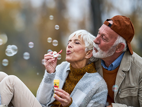 Happy mature couple having fun while blowing bubbles in the park.