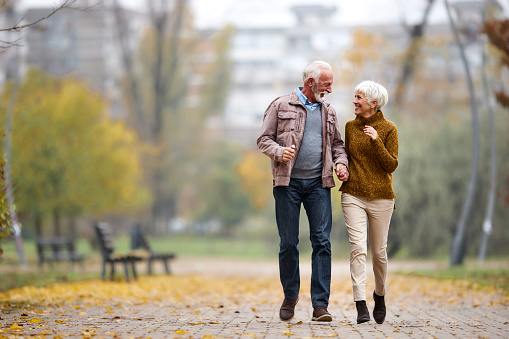 Cheerful senior couple having fun while holding hands and running in autumn day at the park. Copy space.