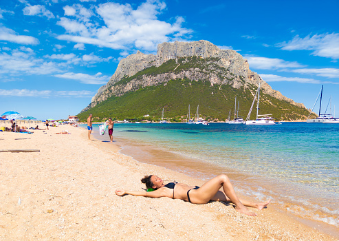 Isola di Tavolara in Sardegna, Italy - 8 July 2022 - The worderful mountain island in Sardinia region, with beach, blue sea, and incredible alpinistic trekking to the summit named Punta Cannone. Here in particular a view of mount from the beach, with people