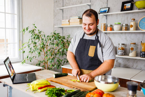 Happy man cooking healthy meal in kitchen Happy man cooking healthy meal in kitchen overweight man stock pictures, royalty-free photos & images