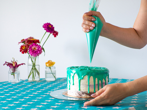 Woman spreading the icing to cover the top of the cake. Home baking, handmade. Free time on quarantine. Confectioner hands topping a cake with mint filling using a pastry bag. Selective focus.