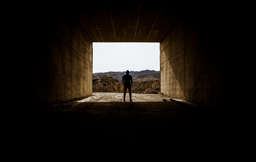 Silhouette of adult man in cowboy hat standing in entrance of a tunnel