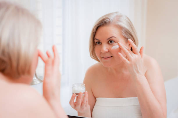 portrait pretty senior woman with hands on her face mirror at home after bathroom skin care after 50-60 years - make up women ceremonial makeup senior women imagens e fotografias de stock