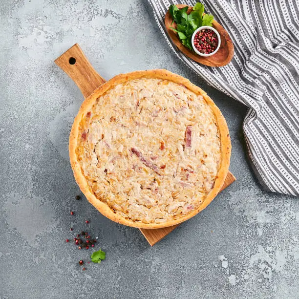 Open pie with bacon and cheese. Quiche lorraine  with cheese on gray stone background. French pie a-la kishin rustic style on stone table. Aesthetic composition with quiche lorraine on wooden board