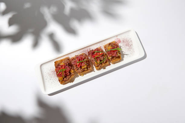 istock Aesthetic composition with shredded beef bruschetta on white background with shadows from flowers. Italian bruschetta with shredded beef and mustard on fine dining in summer. Elegant menu concept. 1422131910