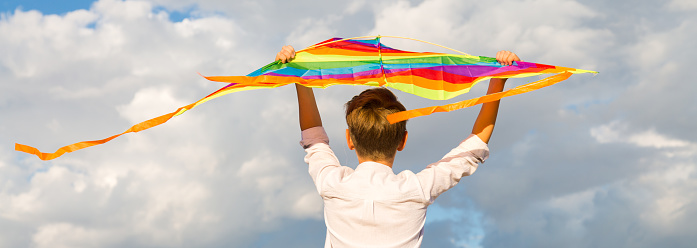 Portrait of a child 8-9 years old with a kite. A blond boy stands and looks into the distance from high mountain.