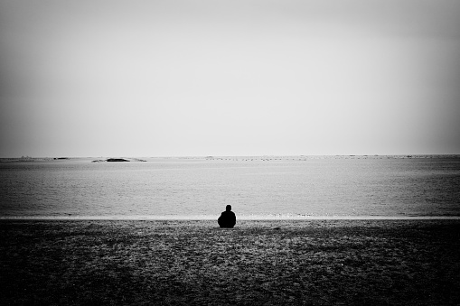 Back view image of a person sitting and looking at the sea