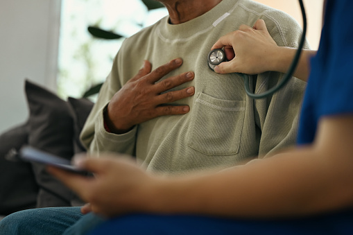 Cropped shot of doctor holding stethoscope checking heart and lungs of elderly male patient.