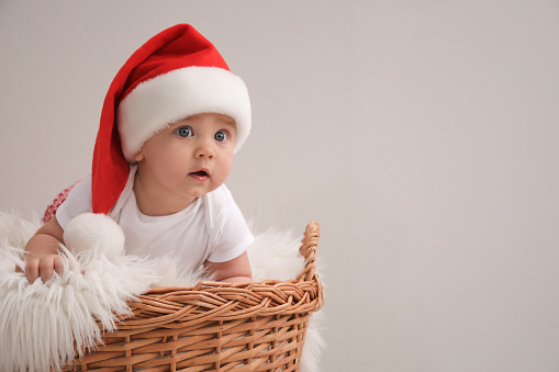 Cute baby in wicker basket on light grey background, space for text. Christmas celebration