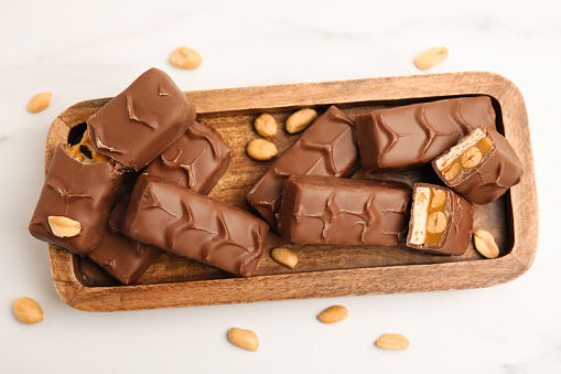 Wooden board of chocolate bars with caramel, nuts and nougat on white marble table, top view