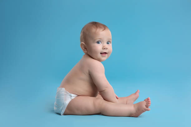 милый малыш в сухом мягком подгузнике сидит на светло-голубом фоне - подгузник стоковые фото и изображения