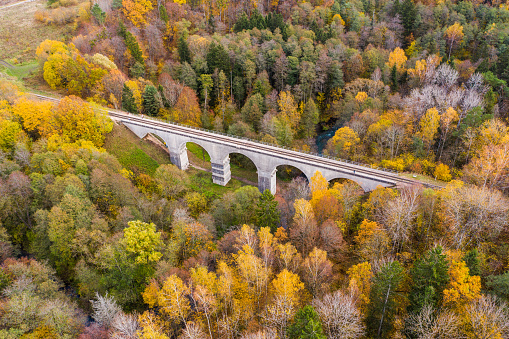 Railway arch bridge surrounded by colorful autumn forest. Aerial drone shot, taken in Romincka Forest (Rominter Heide) natural reserve in Kaliningrad region.