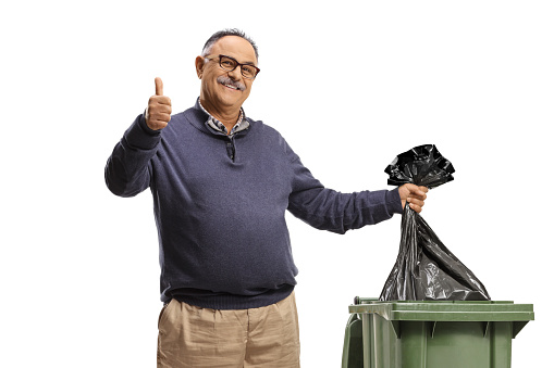Mature man throwing a plastic bag in a bin and gesturing a thumb up sign isolated on white background
