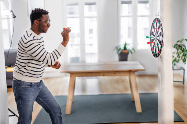 A modern young African is playing darts at home.