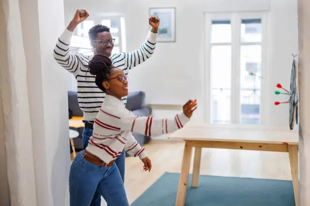 Photo of A cheerful African couple is having a party and enjoying a dart game.