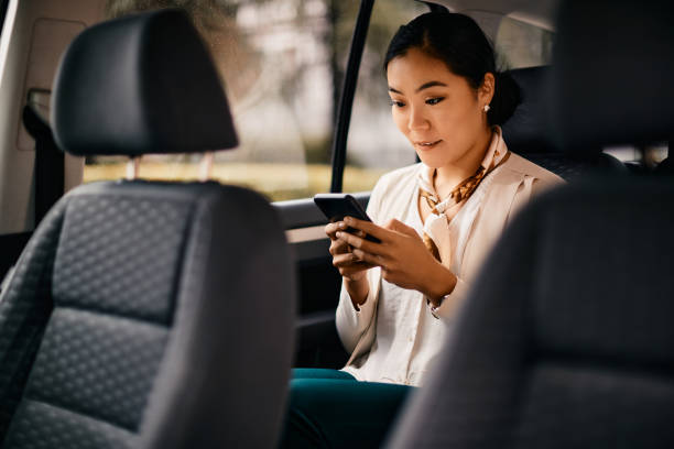 istock Asian female executive using smart phone while driving in a car. 1422144693
